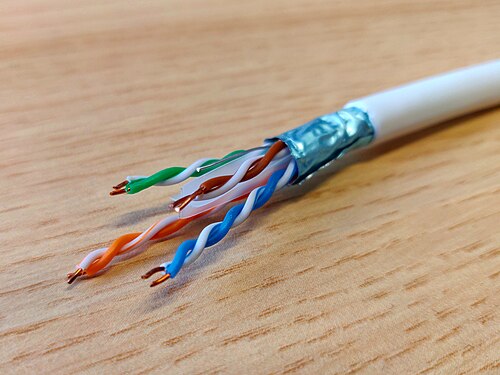 Close-up of a foiled twisted pair Ethernet cable with exposed wires and shielding on a wooden surface in Oxnard, CA.
