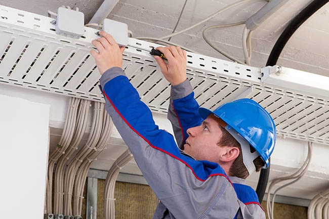Technician installing network cables in a ceiling cable tray for a wireless system in Oxnard, CA.